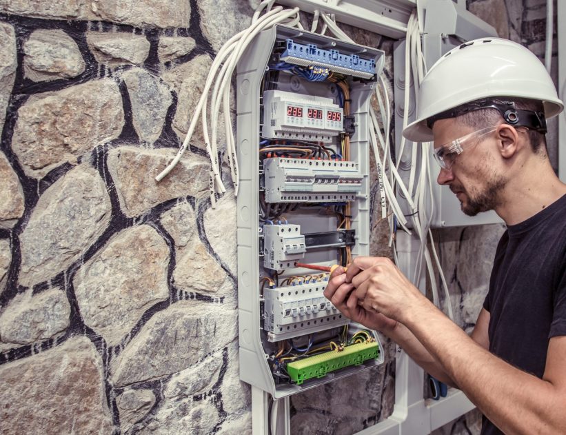 a male electrician works in a switchboard with an electrical connecting cable, connects the equipment with tools, the concept of complex work, space for text